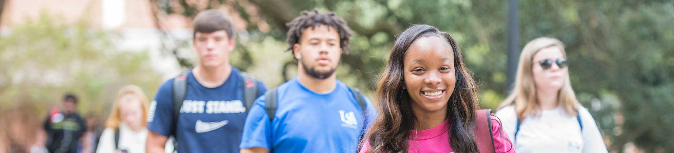 Female student smiling in focus on image with other students walking on USA campus.