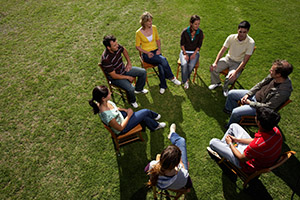 A group of people in a circle sitting outside talking.