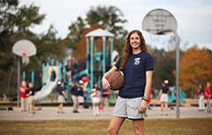 Female student holding basketball in front of court.