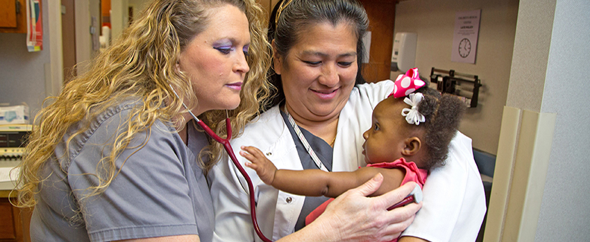 A nurse holding a baby while another nurse listens to the baby's chest