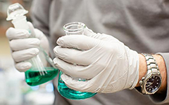Gloved hands holding beakers in lab.