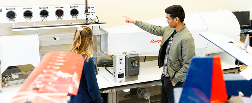 Male student pointing to a machine in mechanical lab.