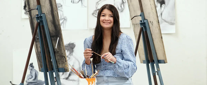 Honors student in paint studio holding a paint brush.