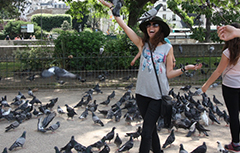 Girls smiling with a black hat on with pigeons all around her