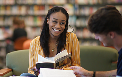 Female student holding a book smiling at a desk in the library
