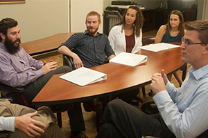 Psychology students and faculty talking around table.