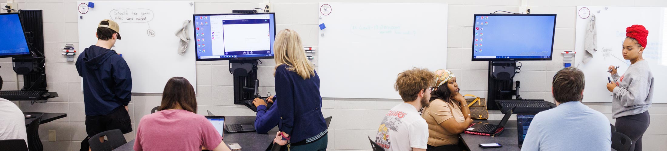 Students and professors working at whiteboard in classroom.