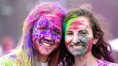 Two female students with their faces covered in color powerder from holi fest.