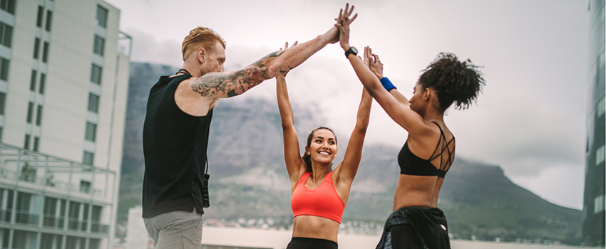 Three people in exercise clothes high fiving each other.