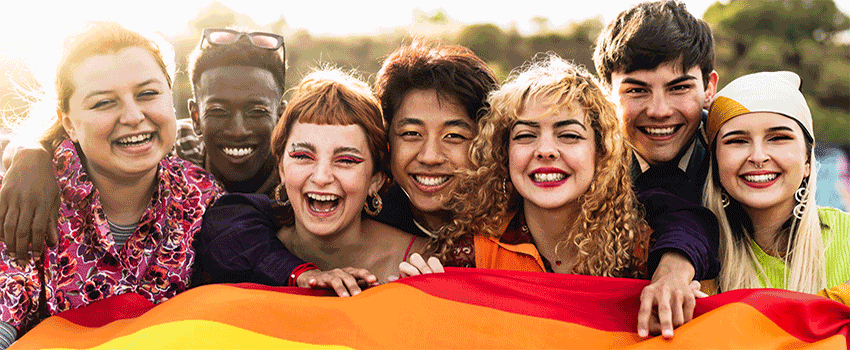 A group of students holding a rainbow flag smiling.