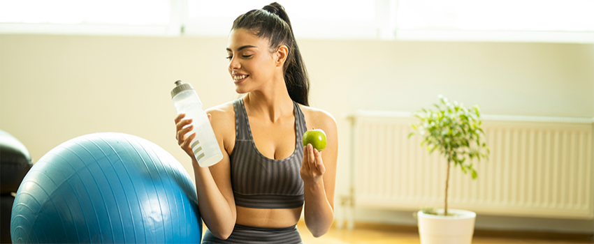 Person in workout room holding water bottle and apple.