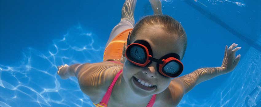Girl in goggles and smiling swimming underwater.