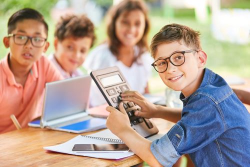 Student holding calculator with other students sitting accross from him at a table.