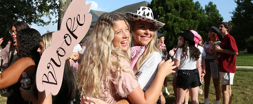 Two girls hugging holding sign.