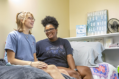 Two female students sitting on their dorm bed laughing