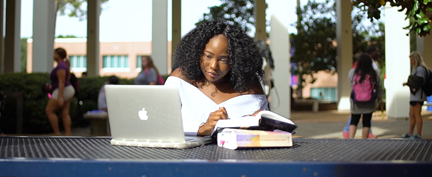 Student sitting outside of Humanities with laptop studying.