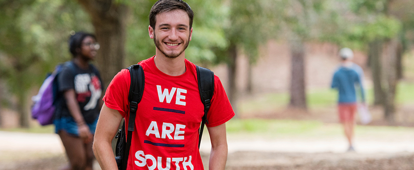 Student smiling with we are south shirt on standing outside on campus.