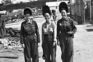 Three women in history smiling wearing work apparel with helmets.