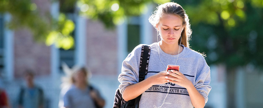 Student walking on campus looking at phone.